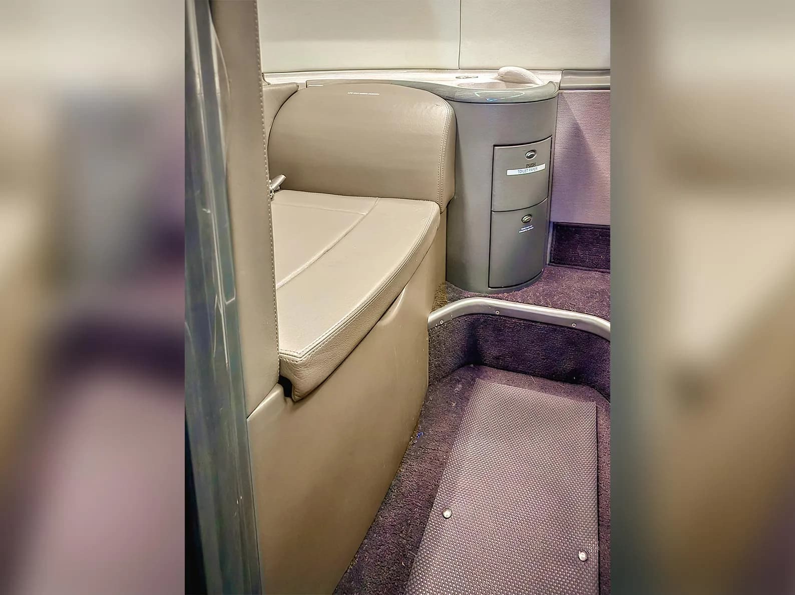 A close-up view of a beige leather seat and a grey storage cabinet inside an aircraft cabin.