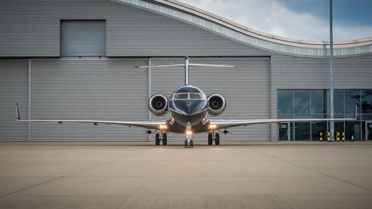 Front view of a black and silver jet parked in front of a hangar.