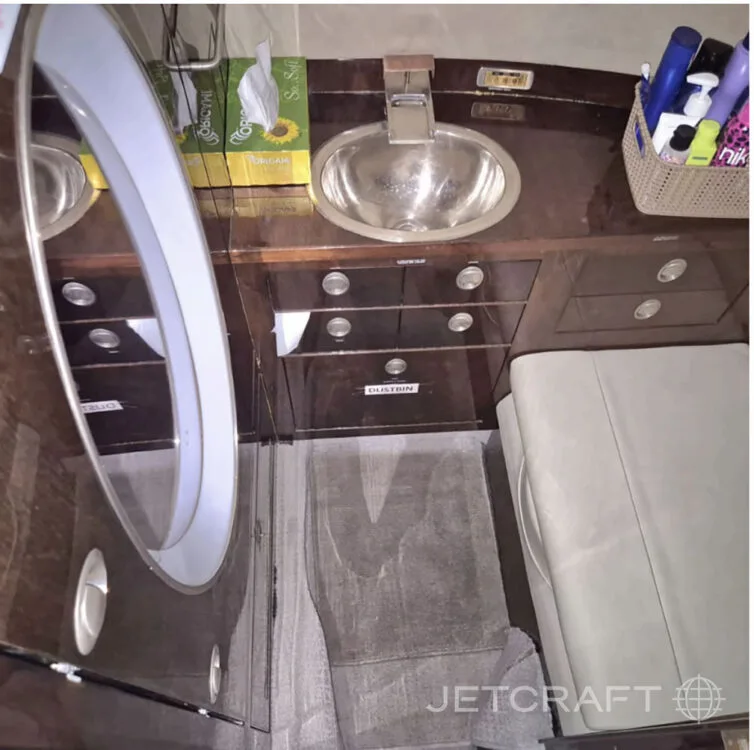 The lavatory or galley area of a business jet, featuring a sink, mirror, and dark wood cabinetry.