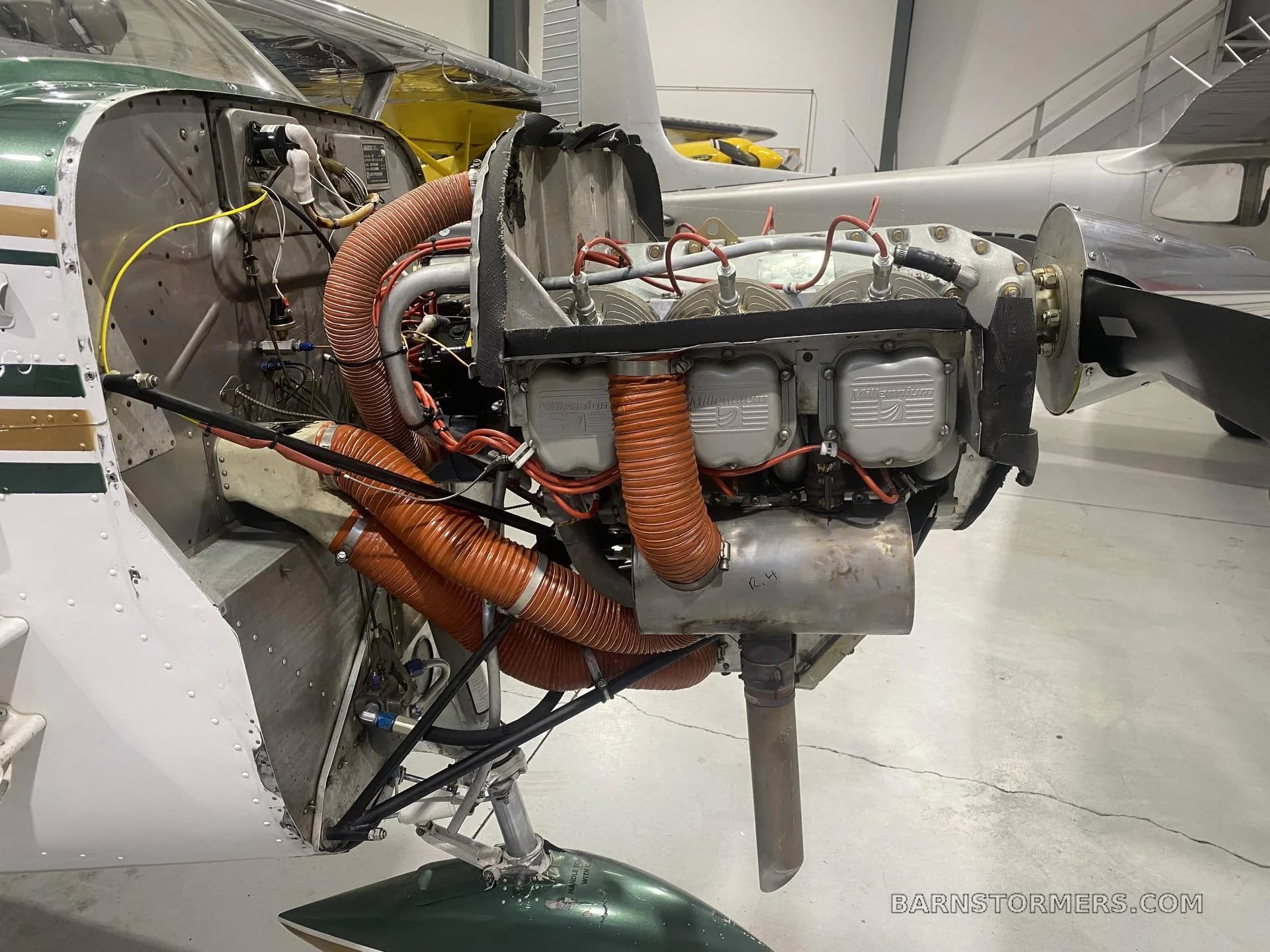 The engine of a white and green aircraft is exposed, showing cylinders, exhaust, and orange air ducts.