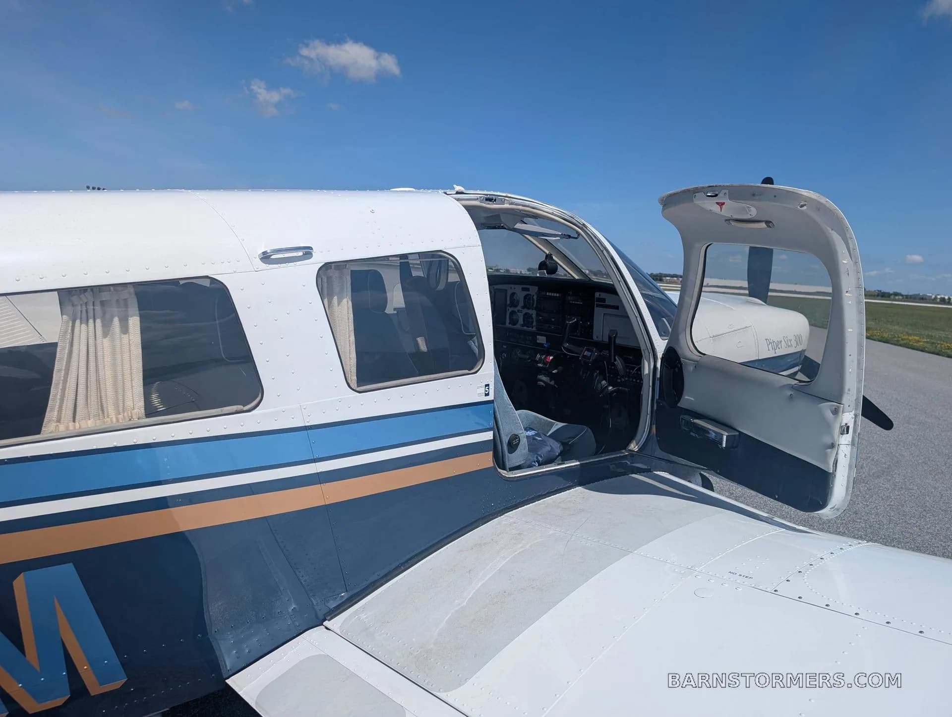 A close-up side view of the Piper Archer 200 aircraft with its passenger door open, revealing part of the cockpit and cabin.