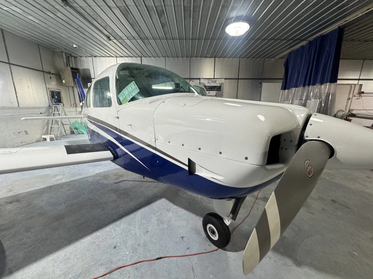 A close-up front-right view of a white and blue single-engine aircraft inside a hangar.
