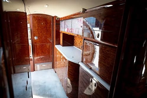 A view of the private jet's galley and lavatory entrance, featuring extensive polished wood paneling and cabinetry.