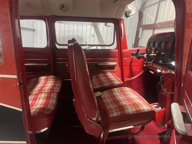 The interior cabin of a small aircraft, featuring red and plaid seats and red side panels, with a glimpse of the cockpit controls.