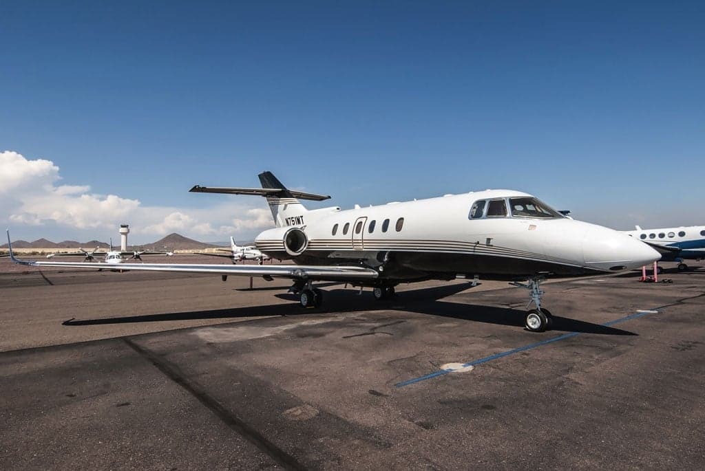 A white and black business jet, N751MT, with gold stripes, parked on an airport tarmac under a clear blue sky.