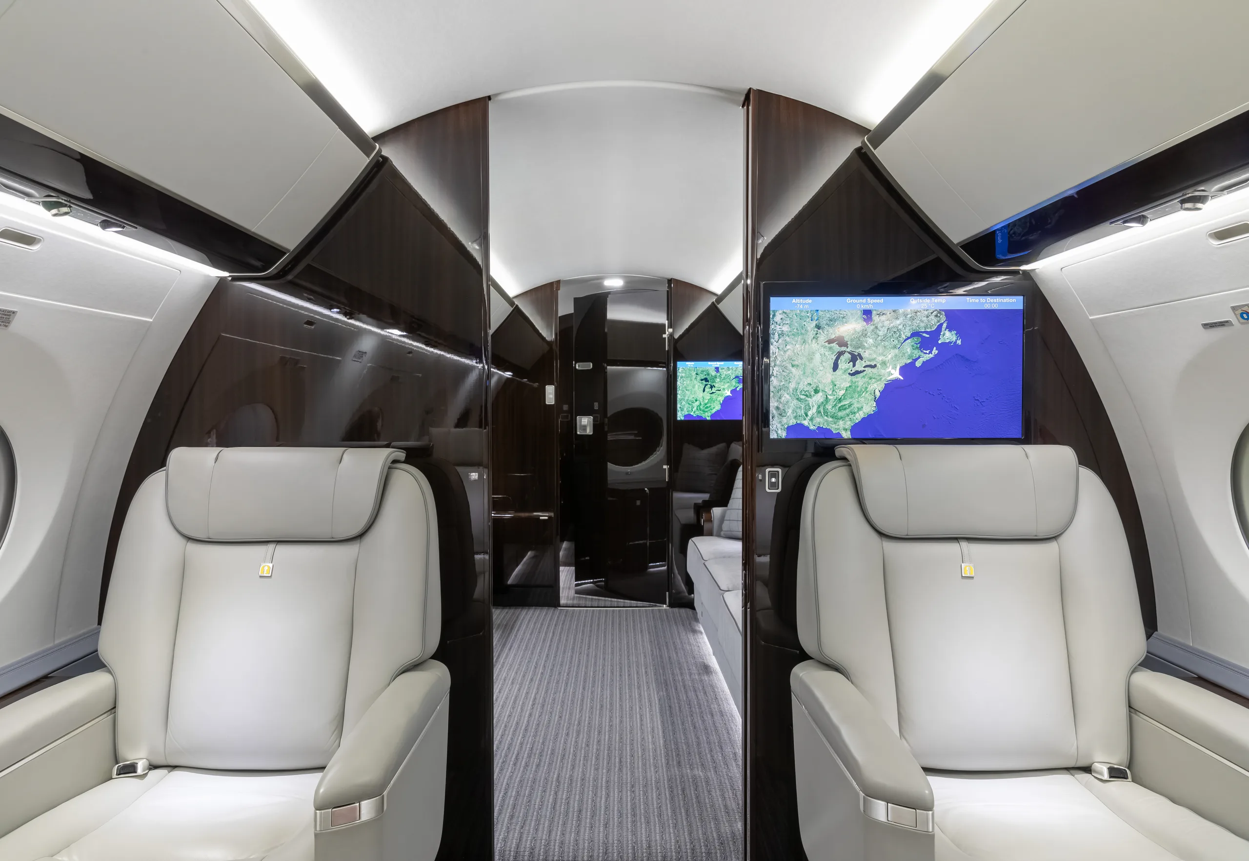 A view inside the private jet cabin, showing two light grey leather seats facing a large screen displaying a map of the East Coast of the United States.