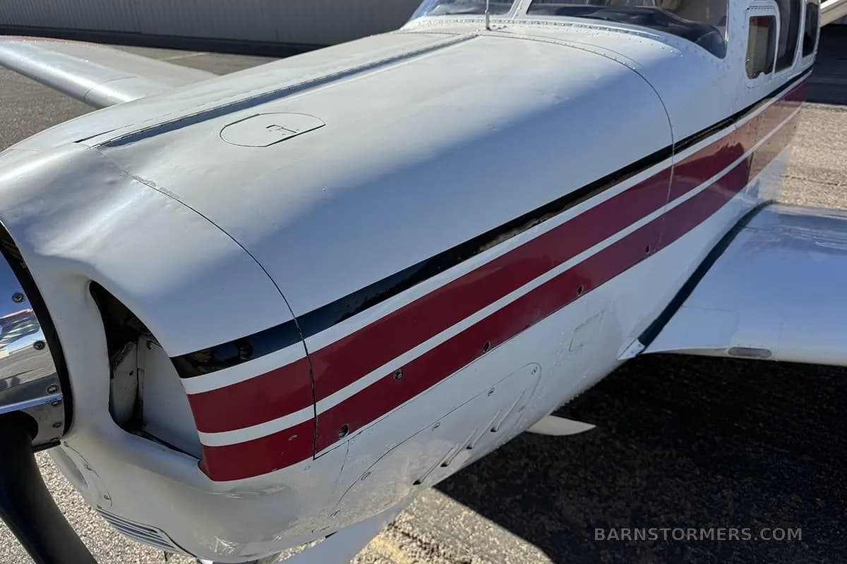 A close-up view of the white fuselage and red stripes on the nose of a single-engine aircraft.