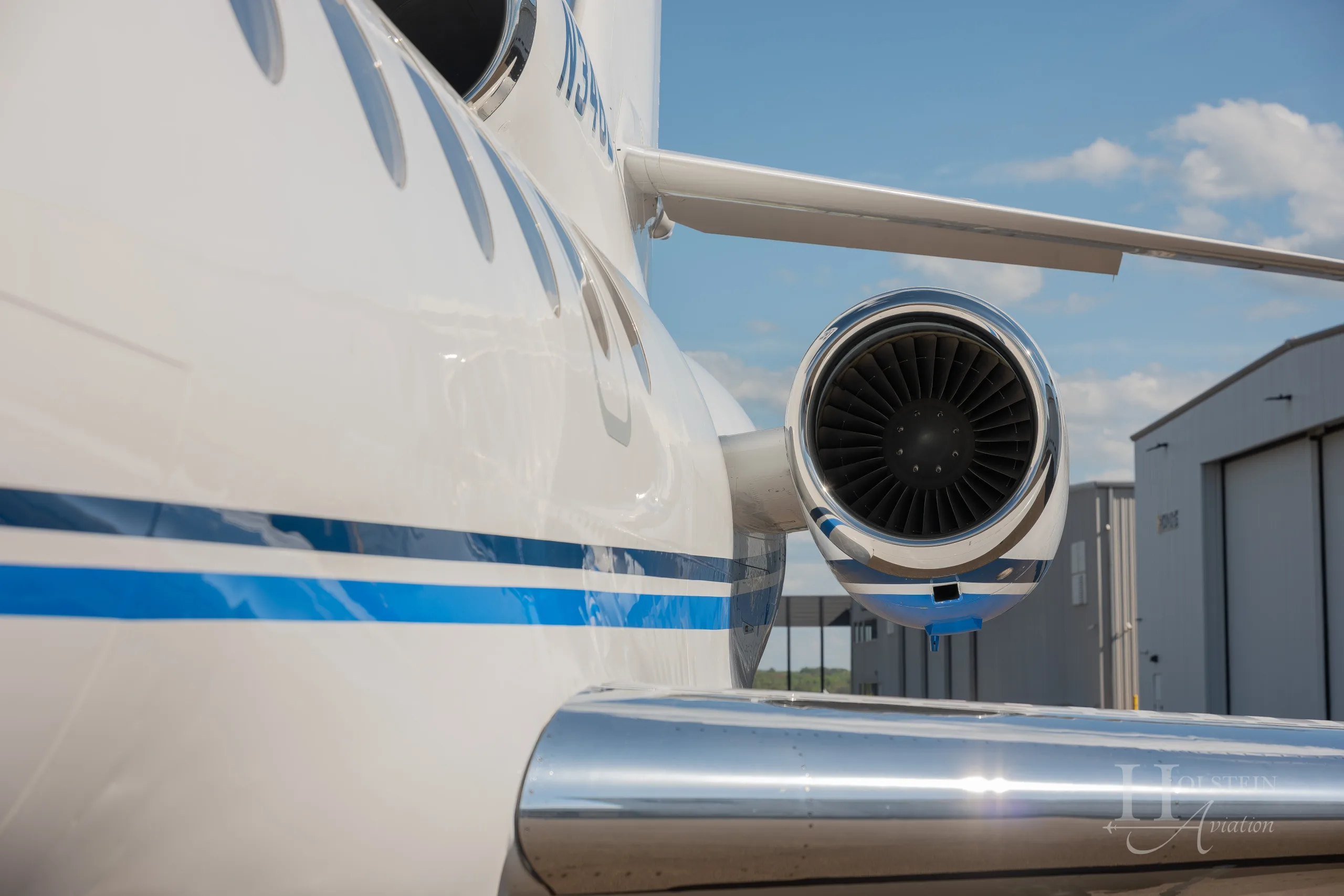 A close-up view of the engine and polished wing of the white Dassault Falcon 900EX, N346EX, with a blue stripe.