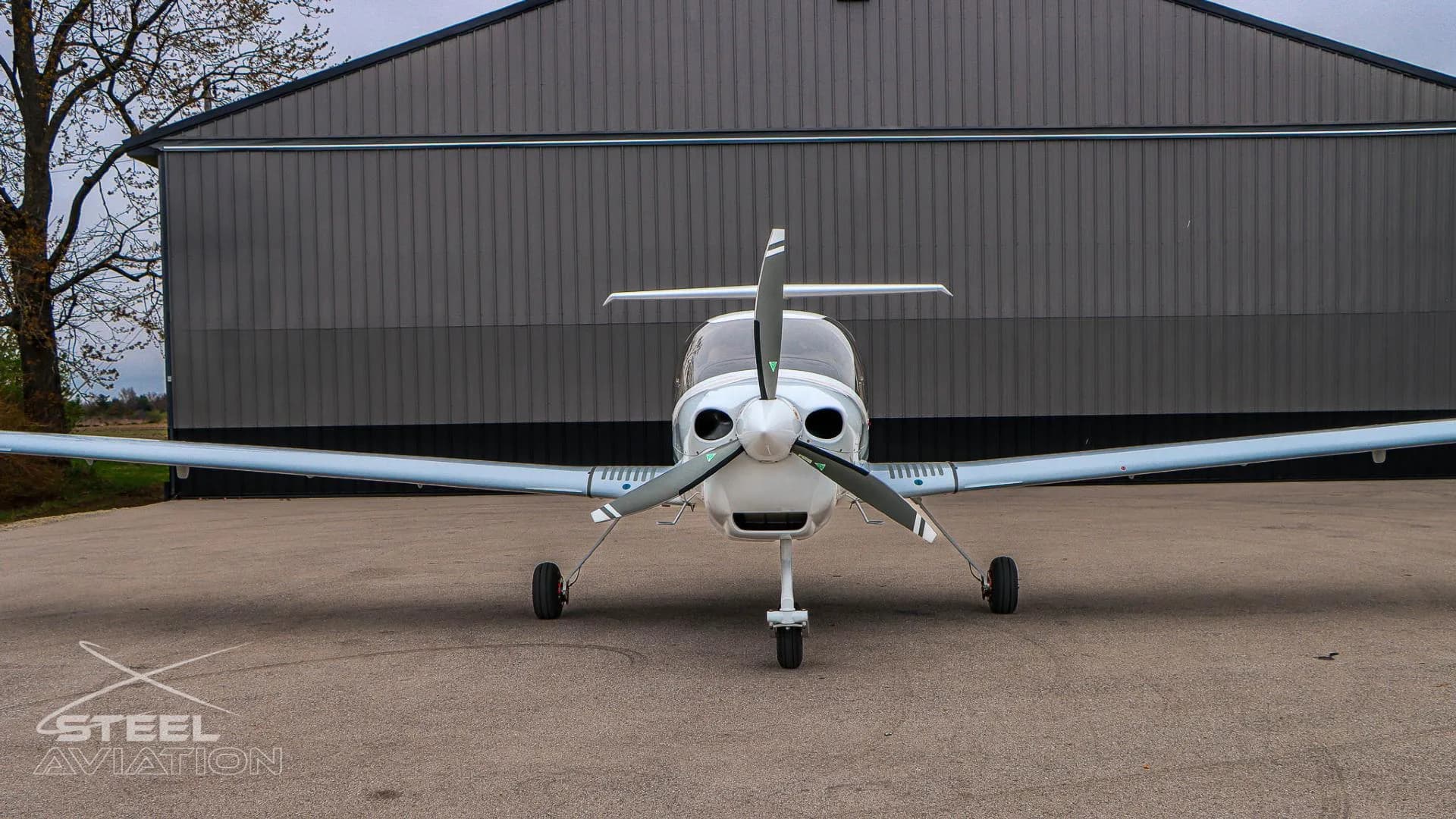 Front view of a white Diamond DA40 NG aircraft with blue and grey stripes parked in front of a hangar.