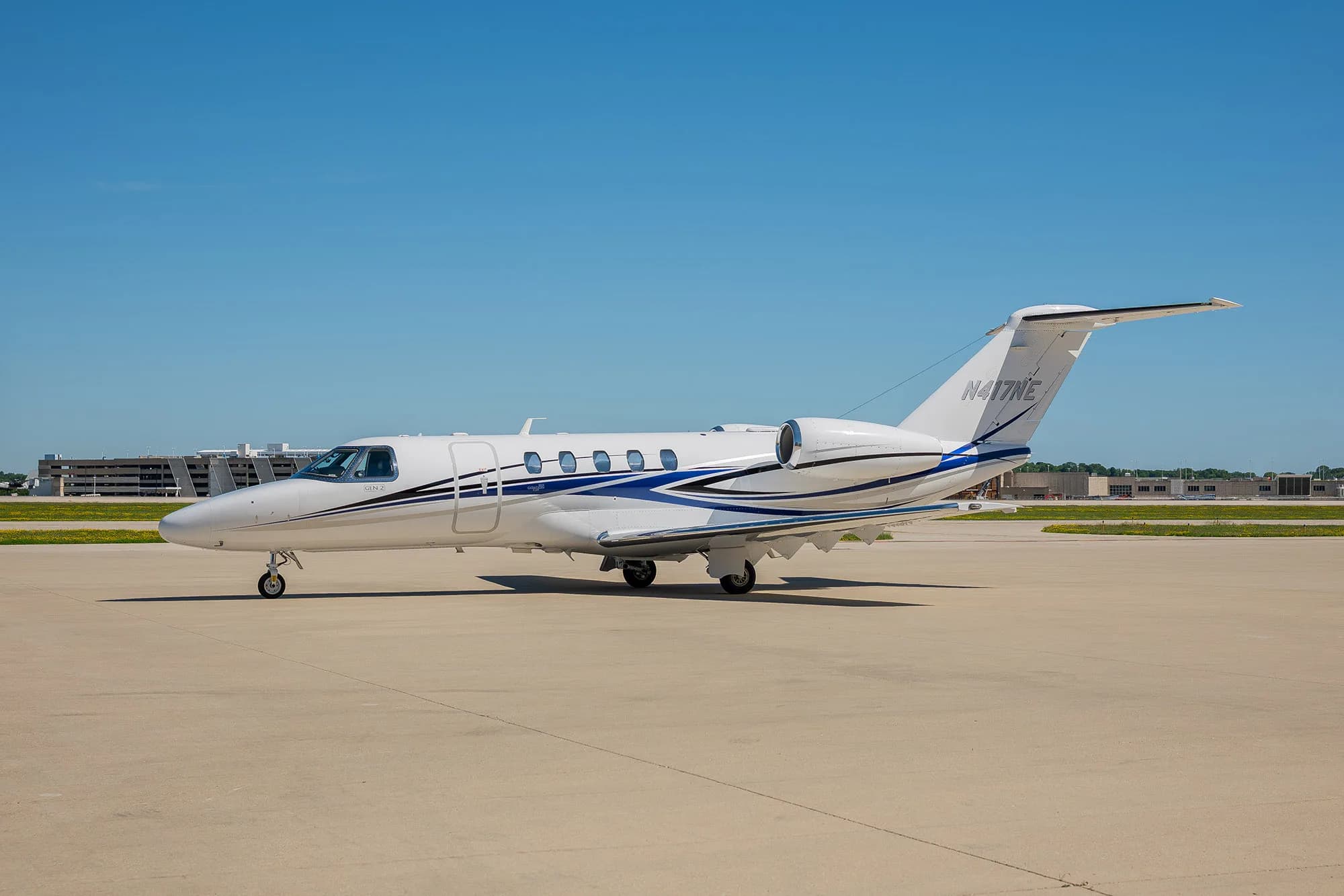 A white Cessna Citation Latitude business jet with blue and grey stripes, tail number N417NE, parked on a tarmac.