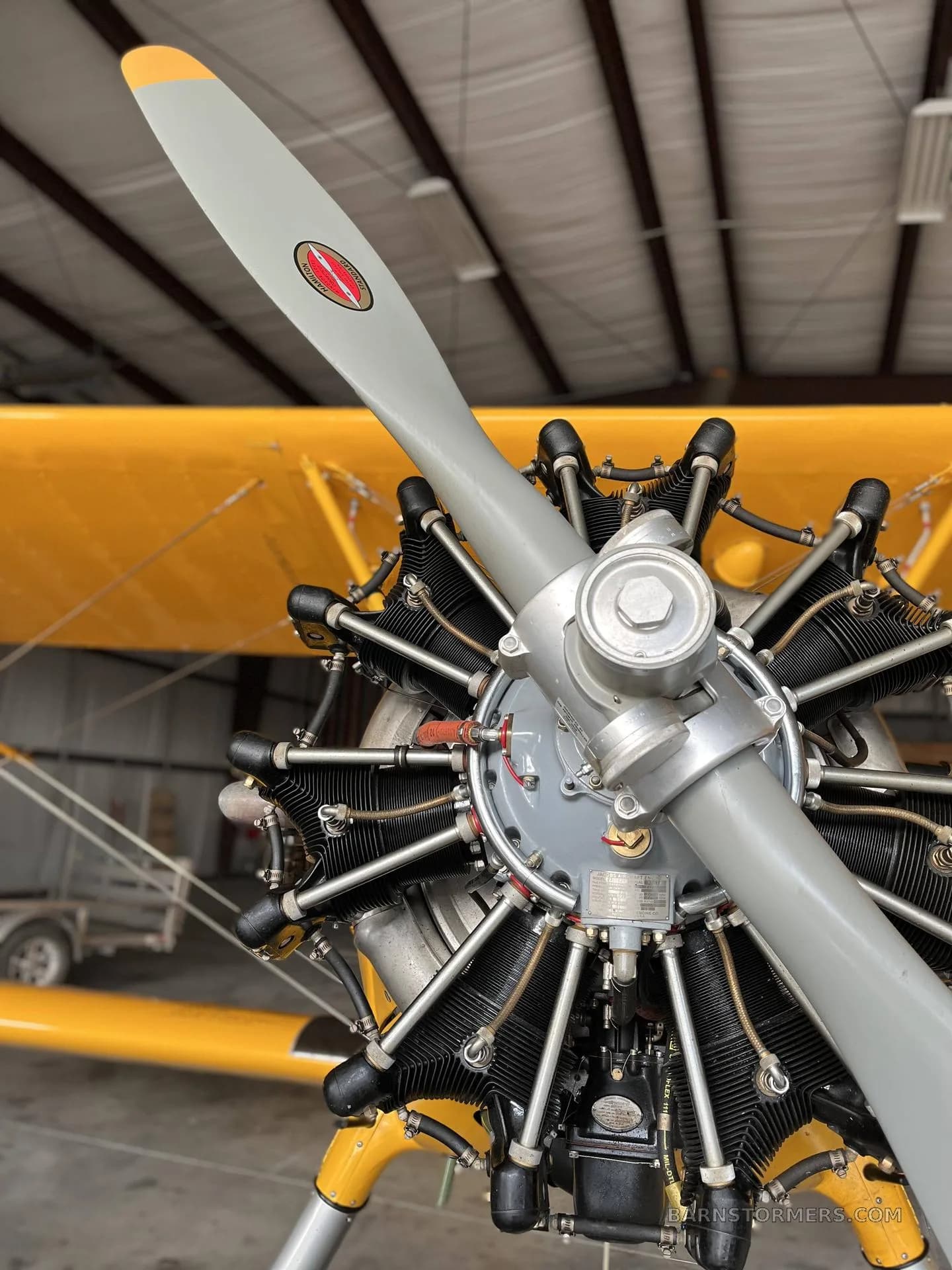 A close-up view of the radial engine and propeller of a yellow biplane inside a hangar.