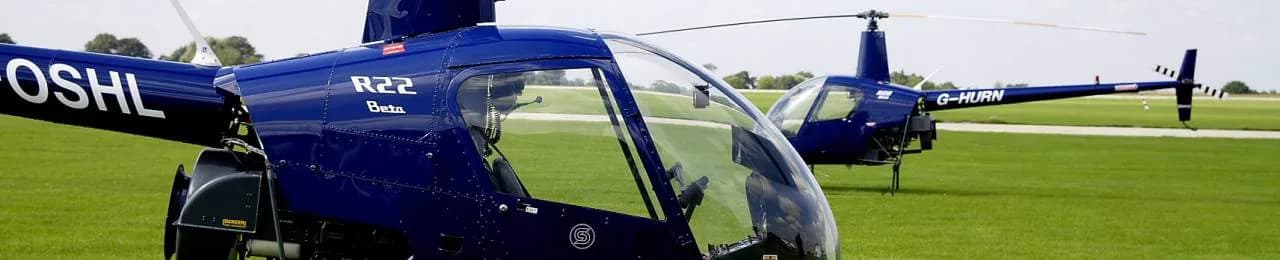 Two blue Robinson R22 Beta helicopters parked on a grassy airfield.
