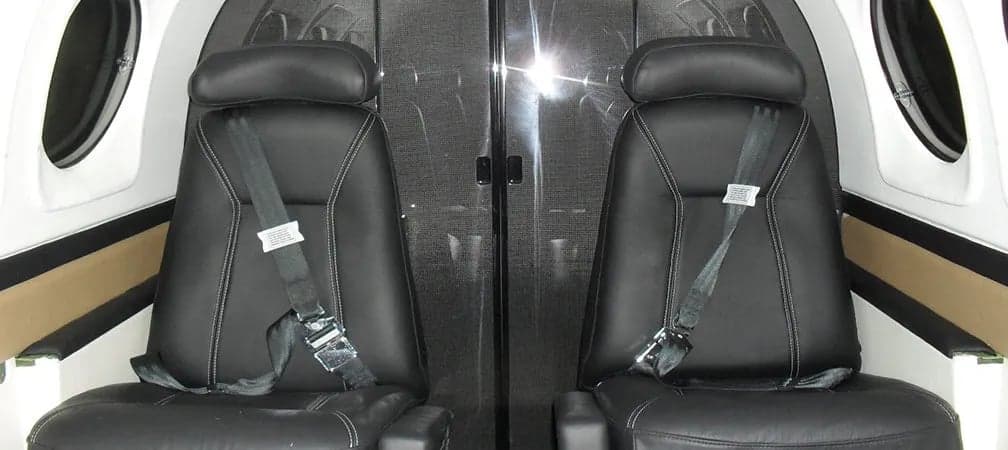 Two black leather seats with seatbelts inside the aircraft cabin.