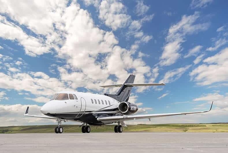 A Hawker jet sits on the tarmac under a partly cloudy sky.