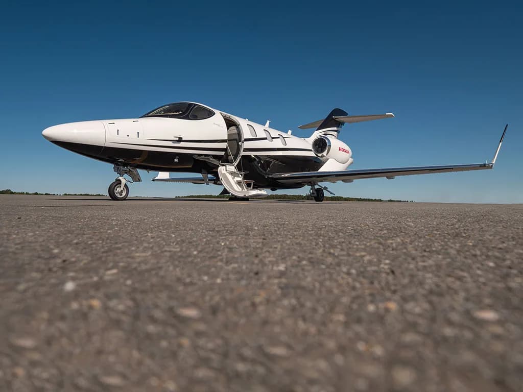 A low-angle view of a white and black HondaJet N301JT parked on an asphalt tarmac with its main door open.