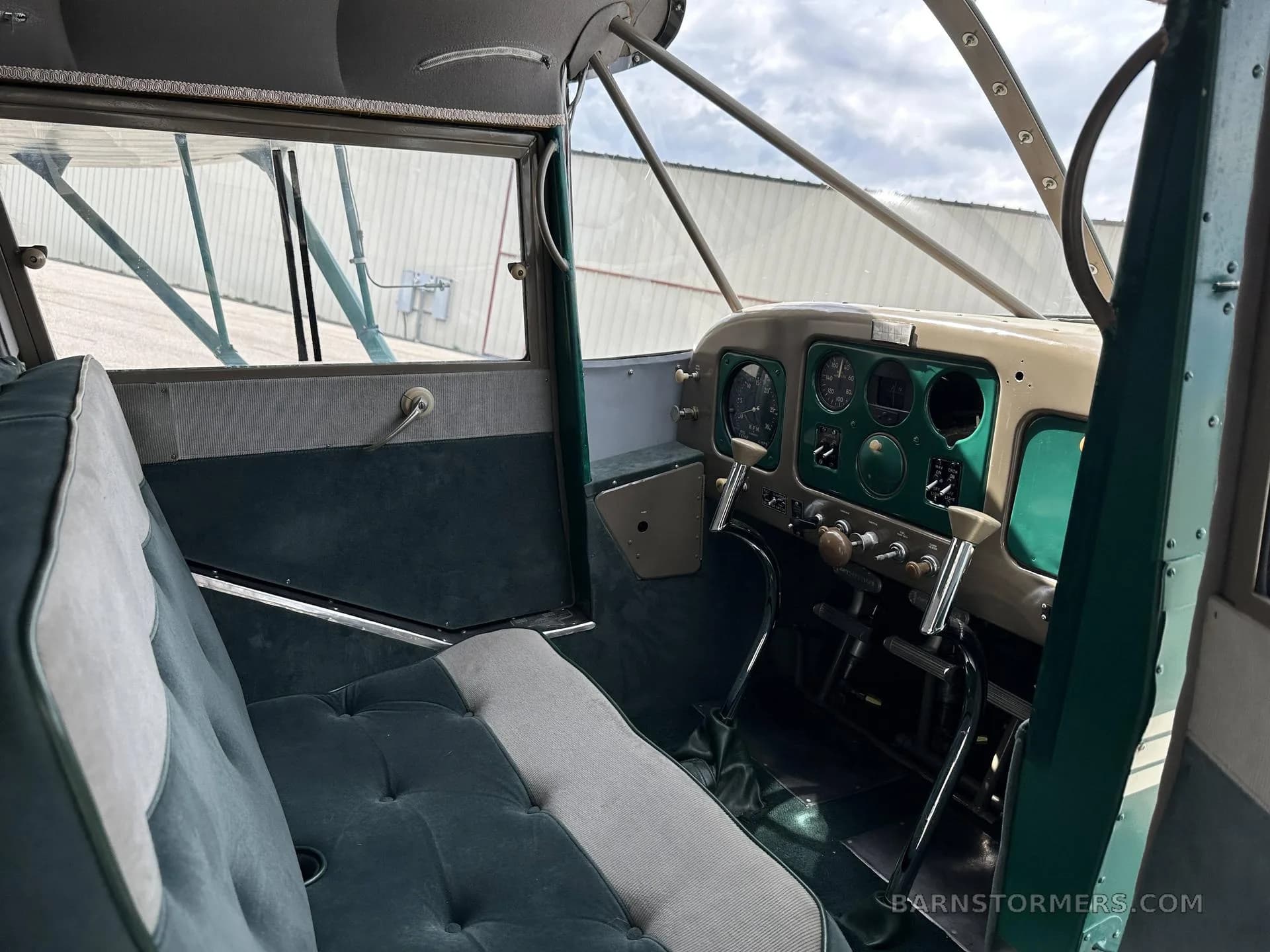 The interior of a vintage aircraft features green upholstered seats and a beige and green instrument panel.