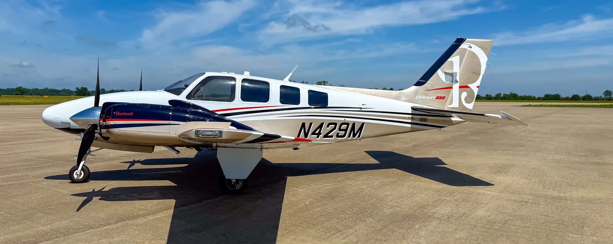 Side view of a white and gold Beechcraft Baron G58 with registration N429M on an airfield.