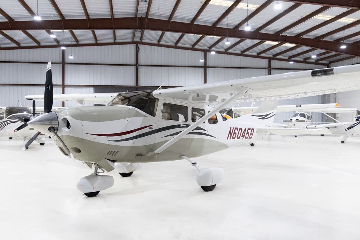 A white and grey Cessna Stationair TC (N6045B) with red and black accents, parked in a hangar.