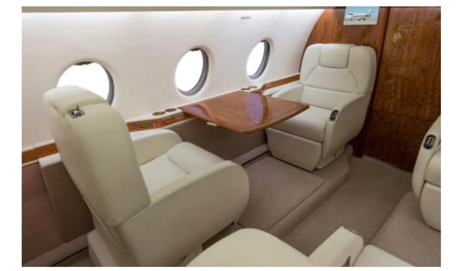 The aircraft's interior features white leather seats and a wooden table.