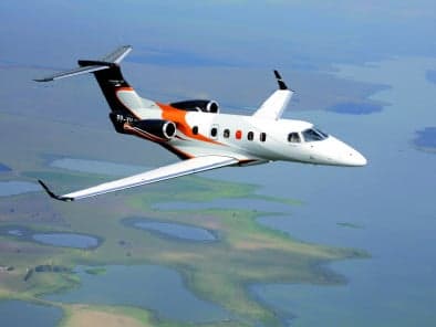 A Phenom 300E aircraft is flying over a body of water.