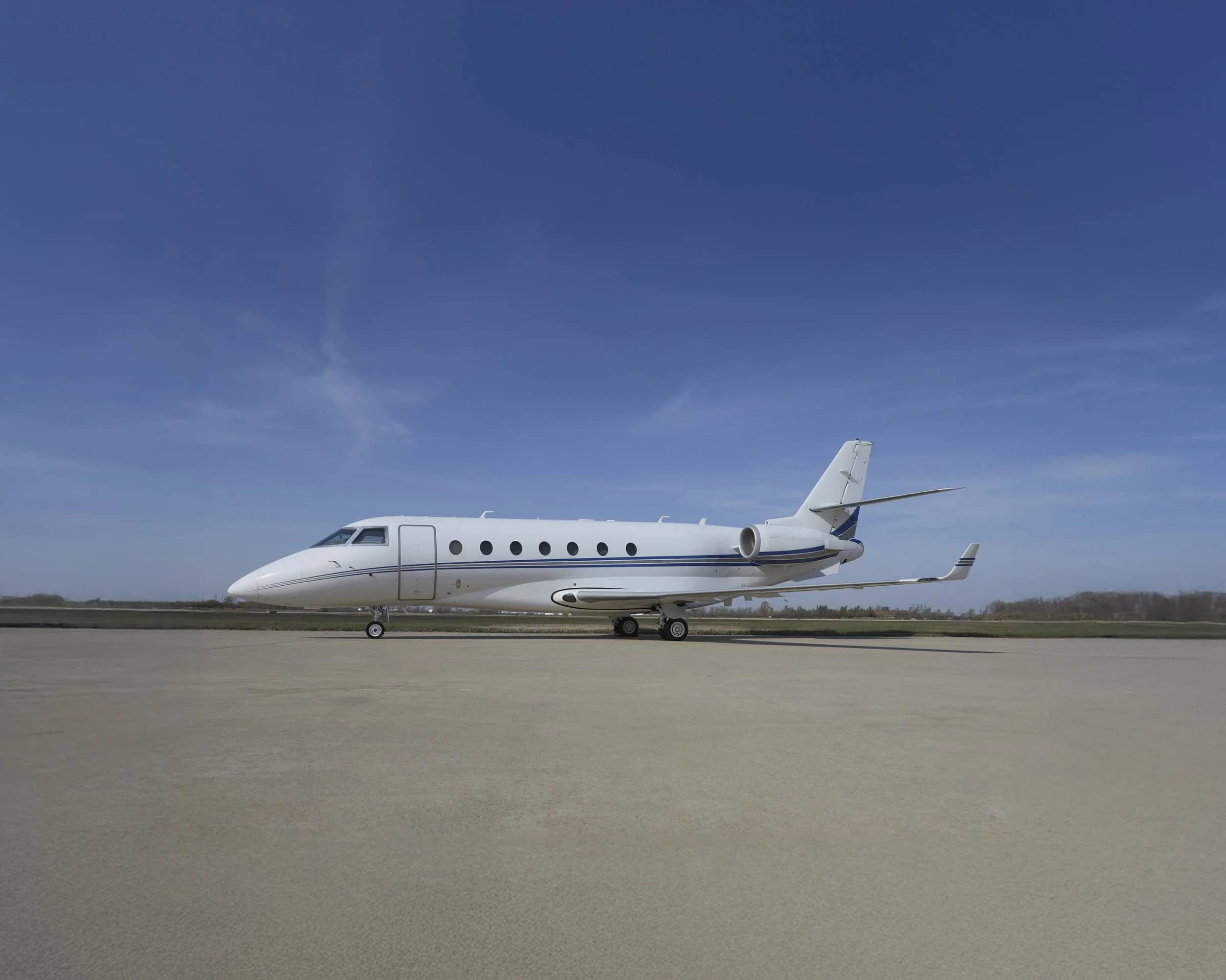 A white and blue Gulfstream jet sits on the tarmac under a blue sky.