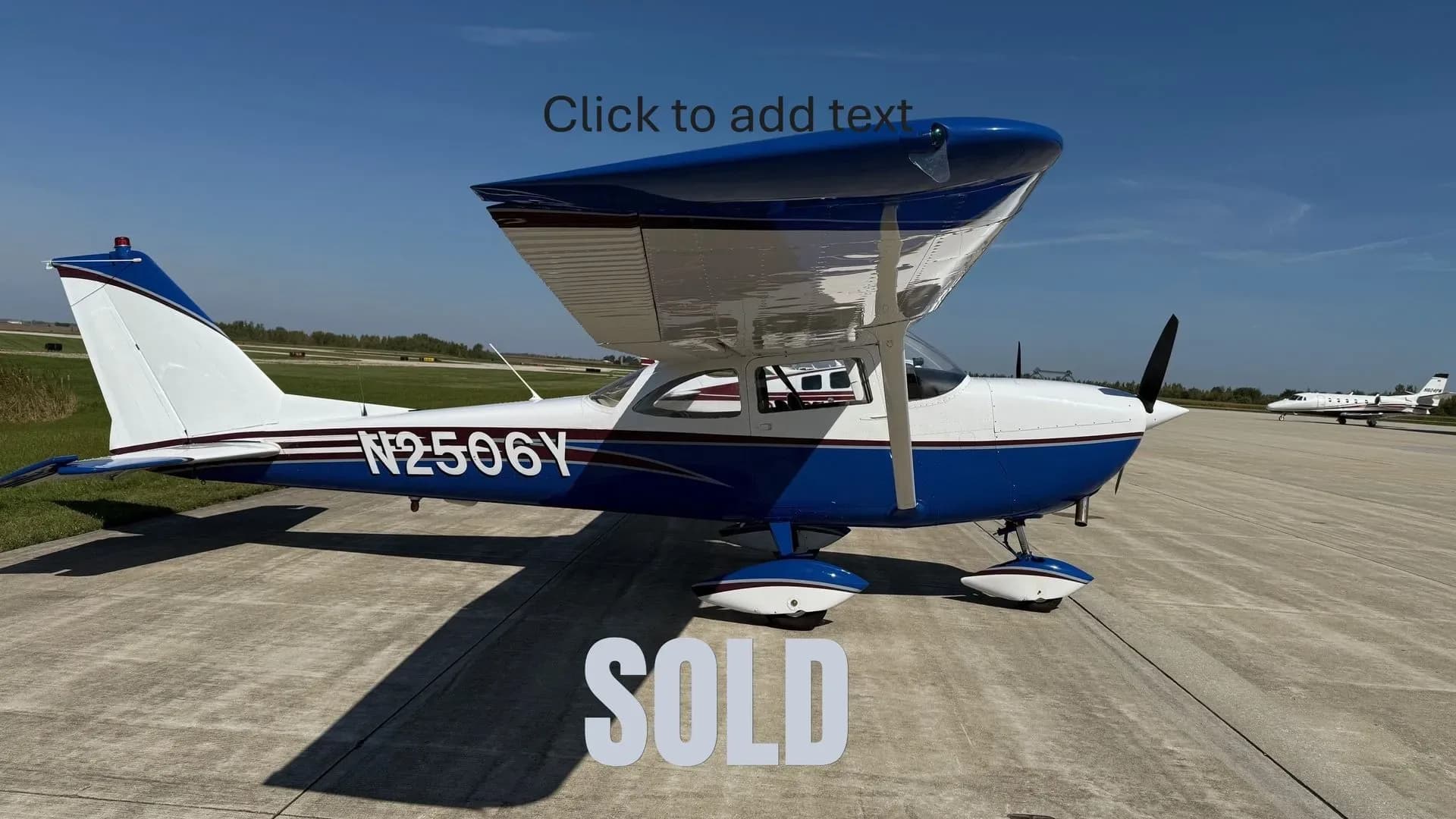 A blue and white high-wing single-engine propeller aircraft, N2506Y, parked on an airfield with a private jet in the background.