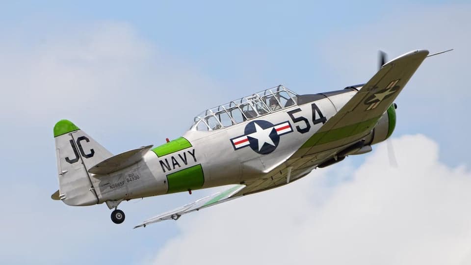 A silver and green T-6 Texan aircraft flying in the sky.