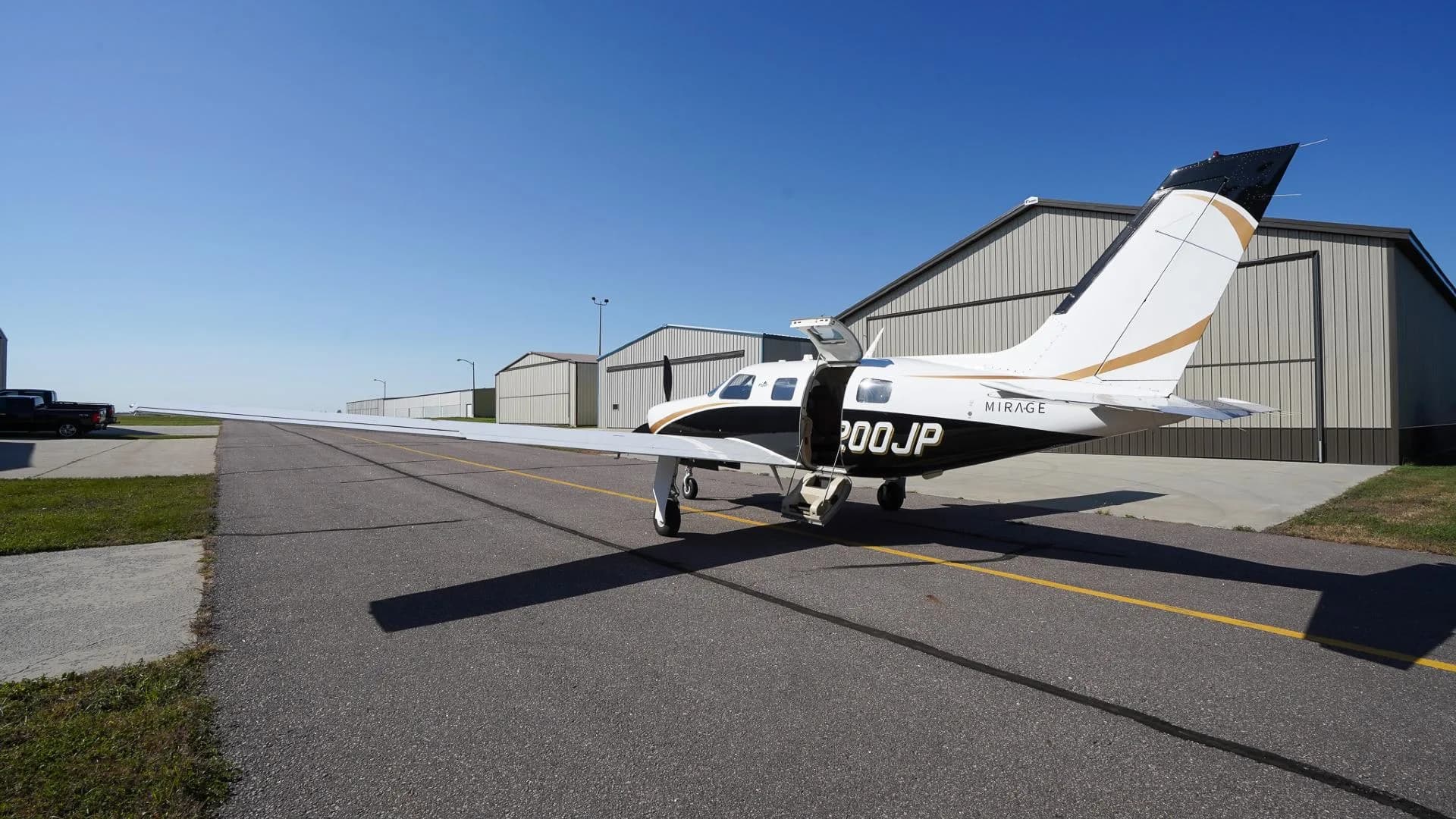 A rear-side view of a white and black Piper Mirage N200JP with gold accents and open cabin door on an airfield.
