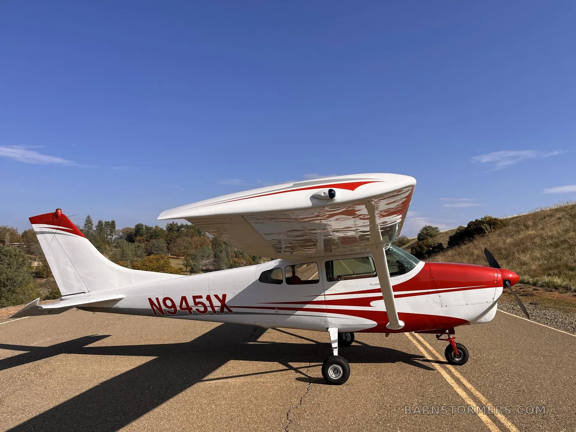 A white and red Cessna 182 aircraft with registration N9451X parked on an asphalt surface, viewed from the front-right.