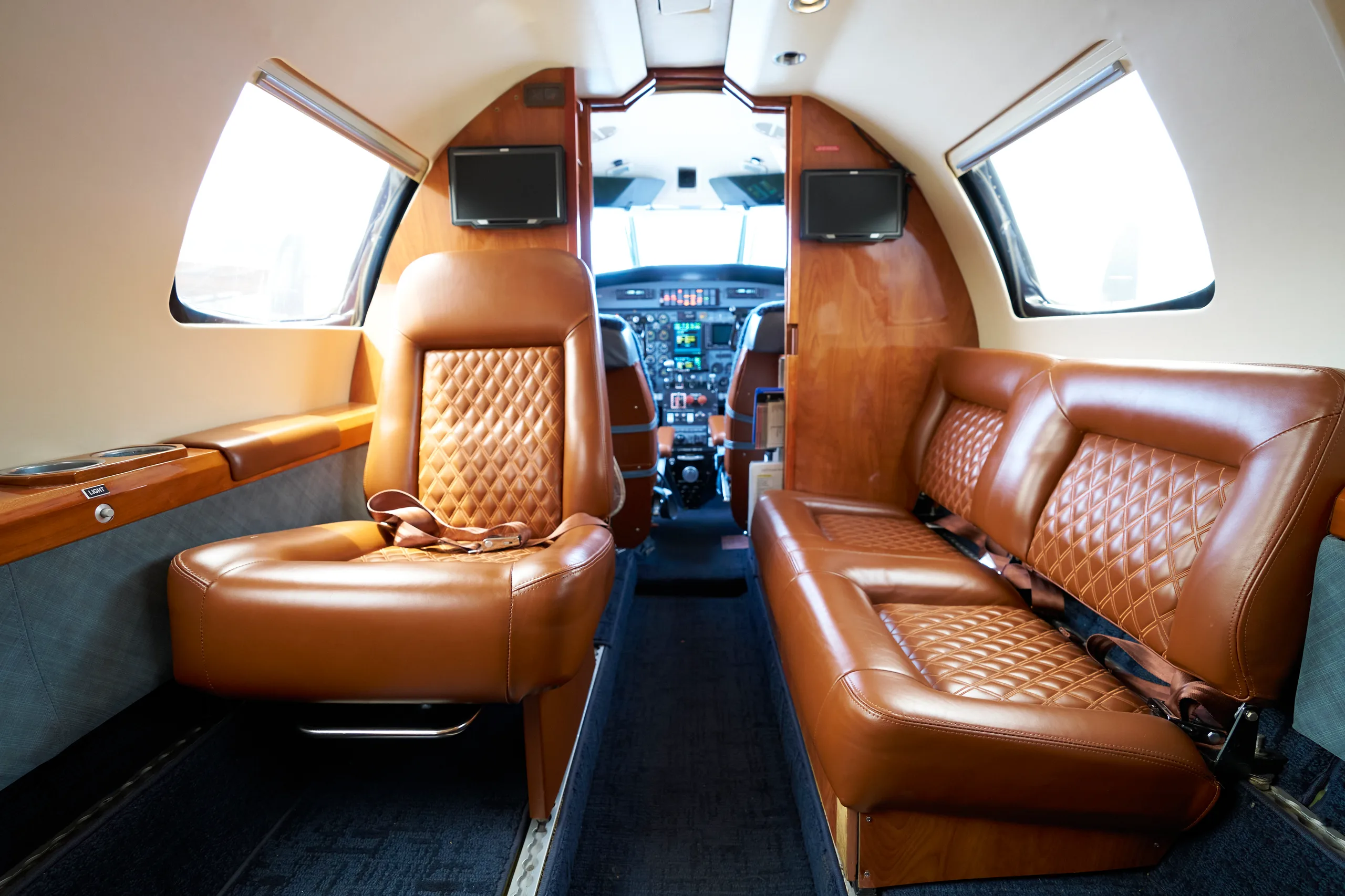 The aircraft's cabin interior features brown quilted leather seats and wood paneling, looking towards the cockpit.