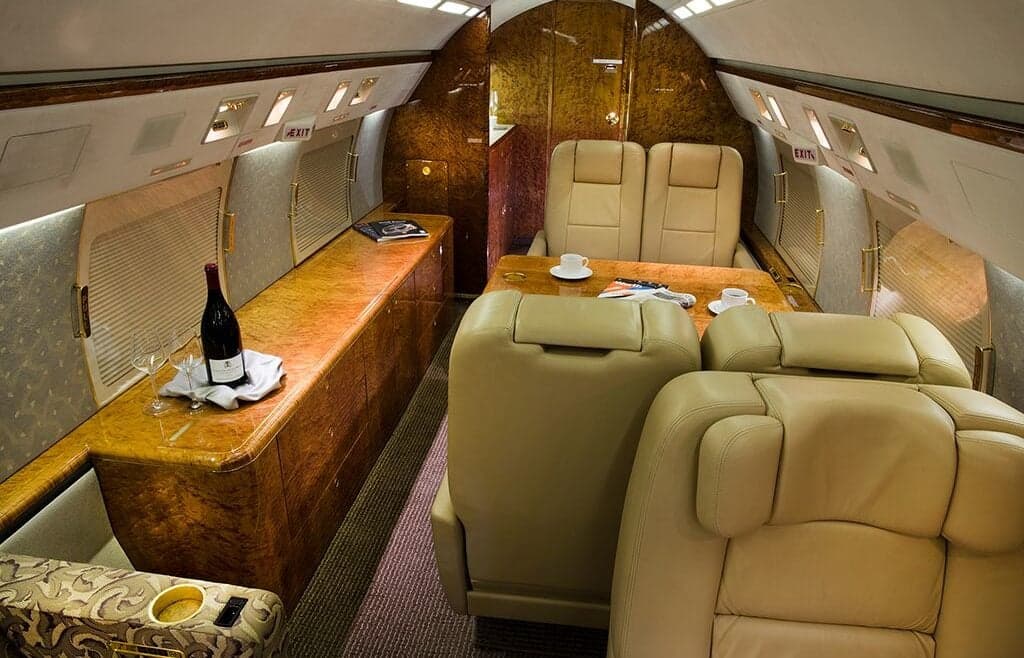 Luxurious interior of the aircraft with leather seats, a wooden table, and a bottle of wine.
