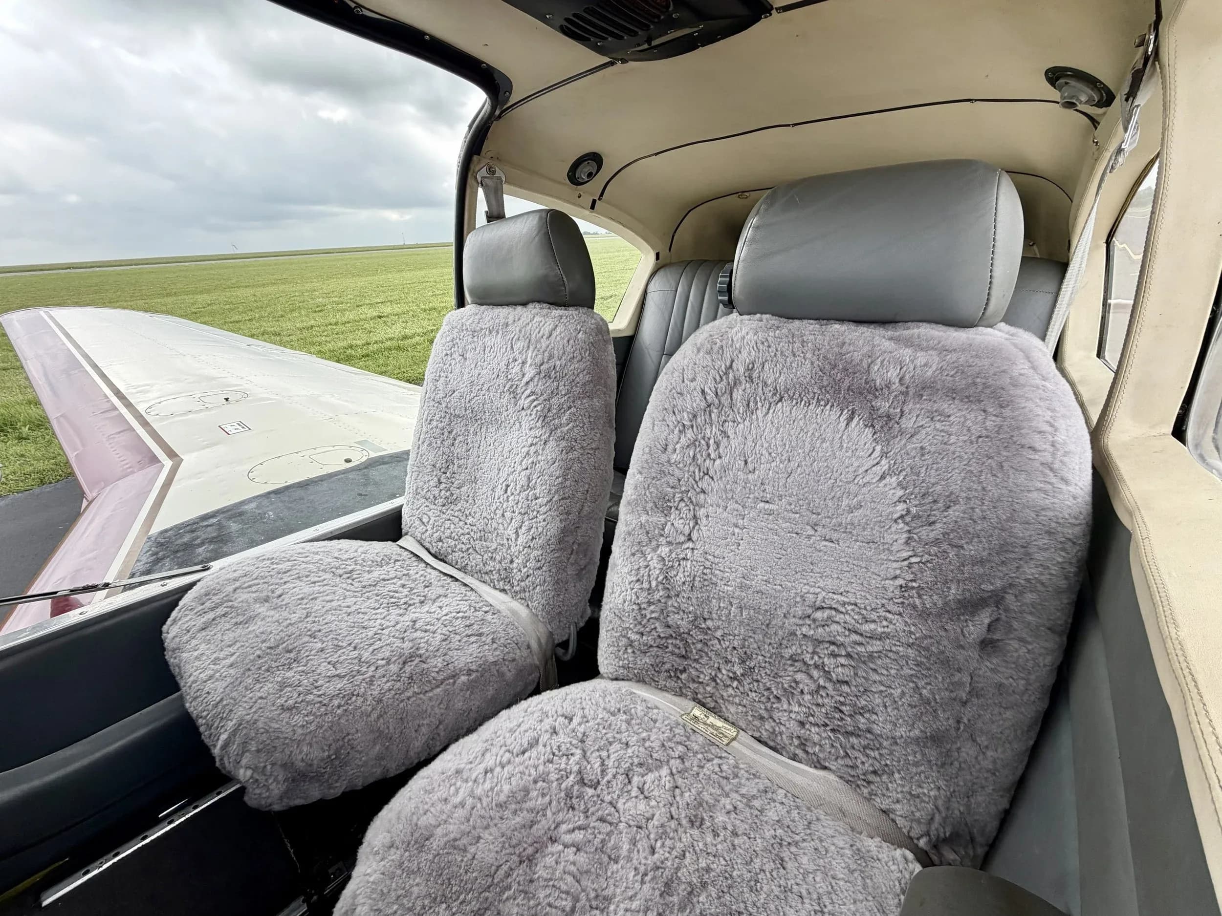 The front cabin seats of a Piper Comanche N7727P covered in grey sheepskin covers.