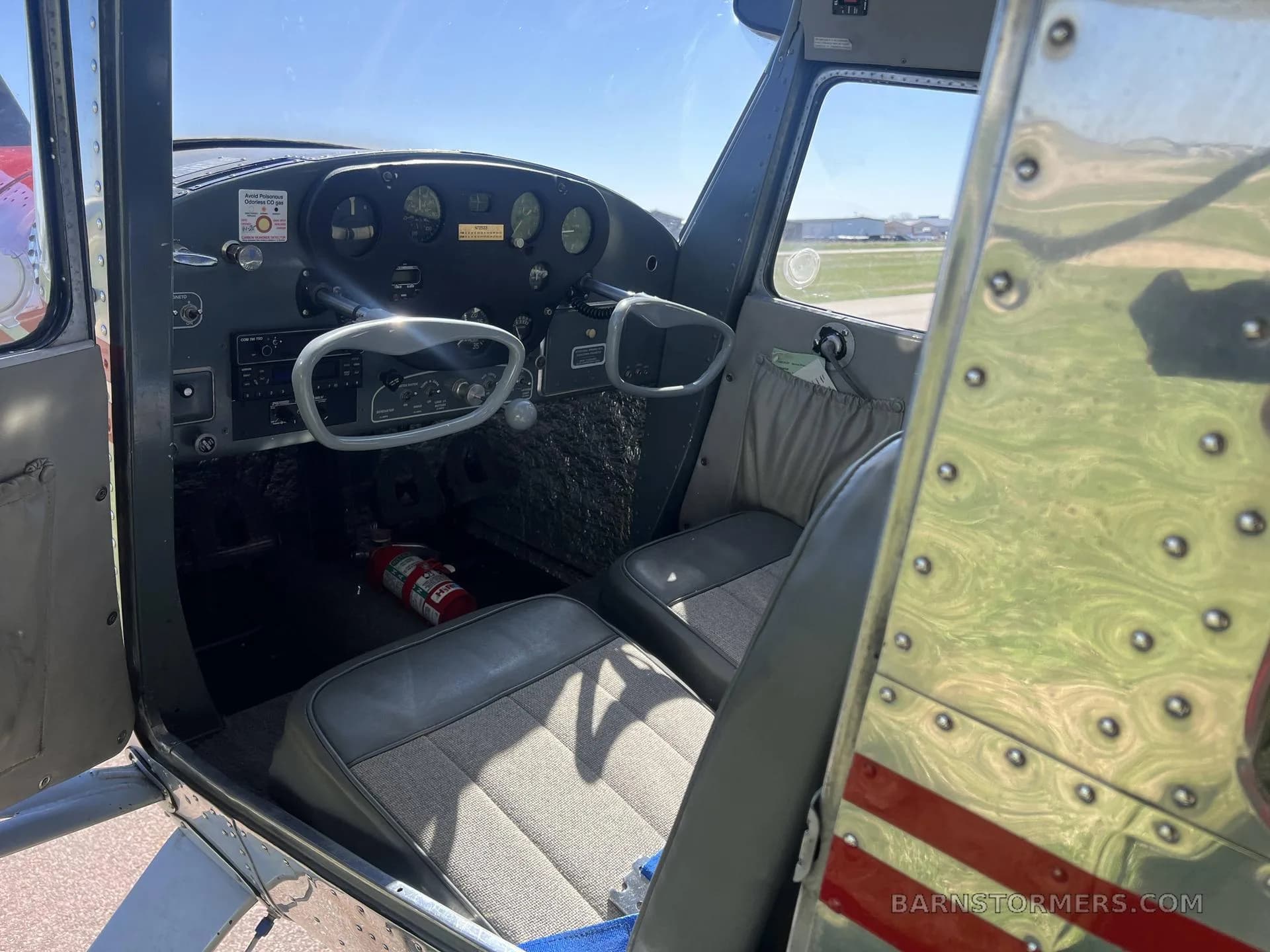 The cockpit interior of a Cessna 140, showing the instrument panel, dual yokes, and two grey fabric seats.