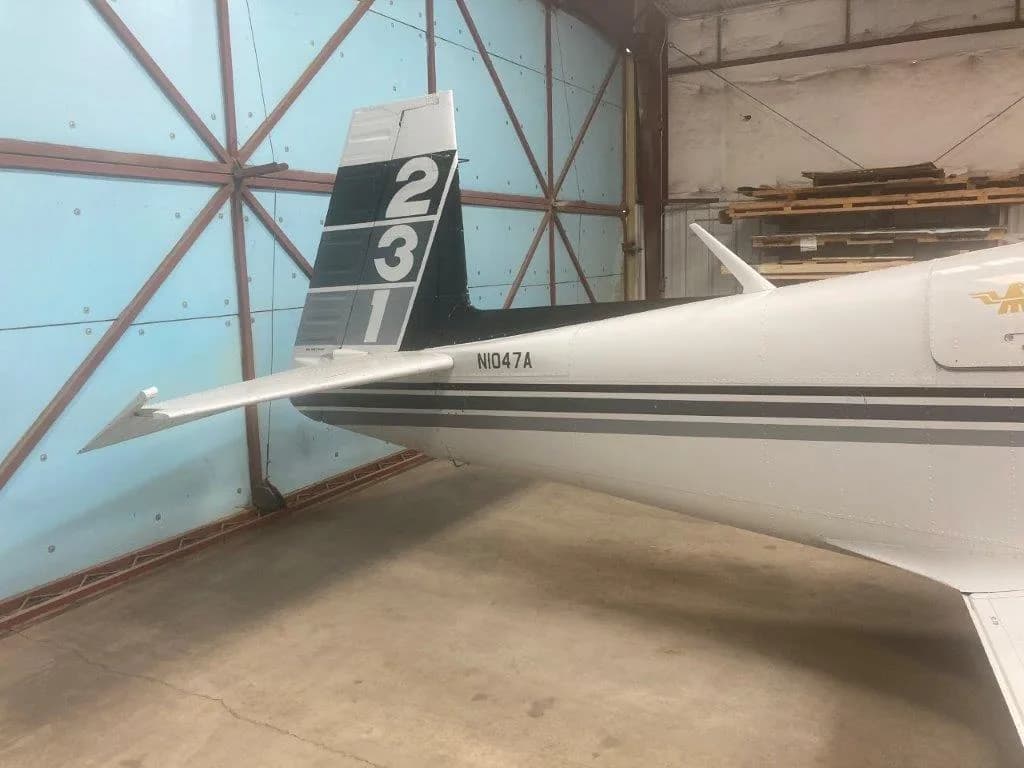 Close-up of the tail of a white and black Grumman American AA-5 Traveler aircraft, N1047A, inside a hangar.