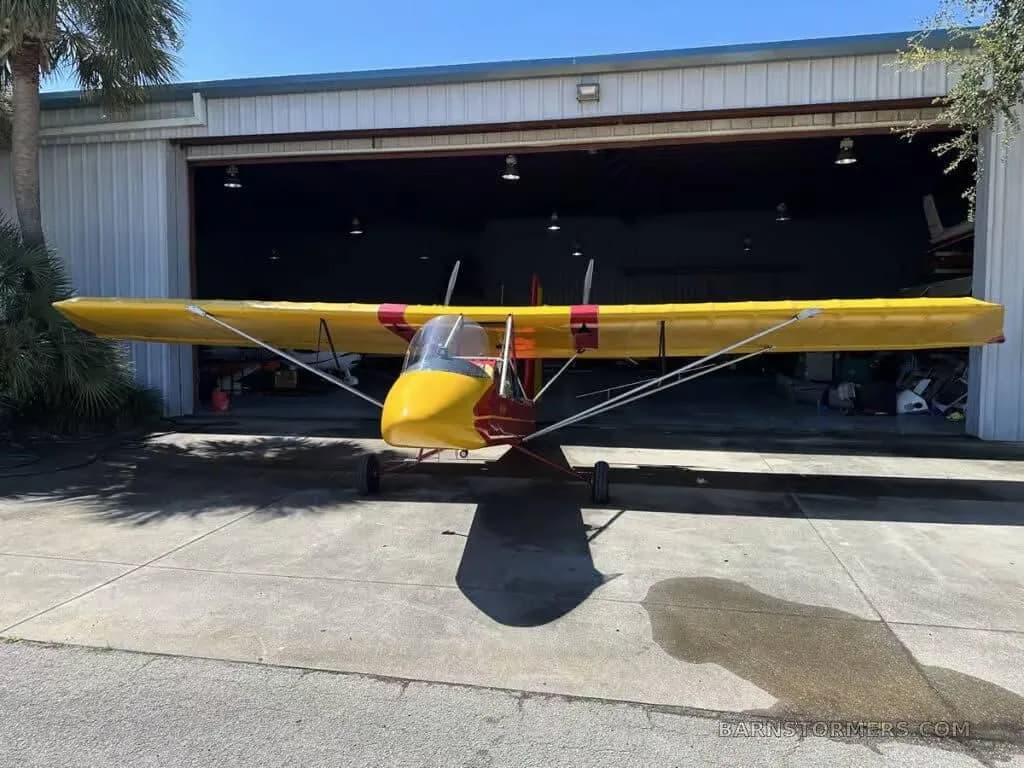 Front view of a red and yellow Air-Cam aircraft parked in front of a hangar.