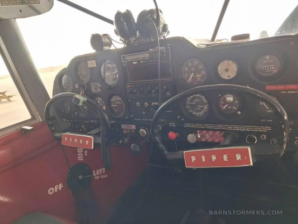The cockpit of a Piper aircraft, showing the instrument panel, yokes, and red interior trim.