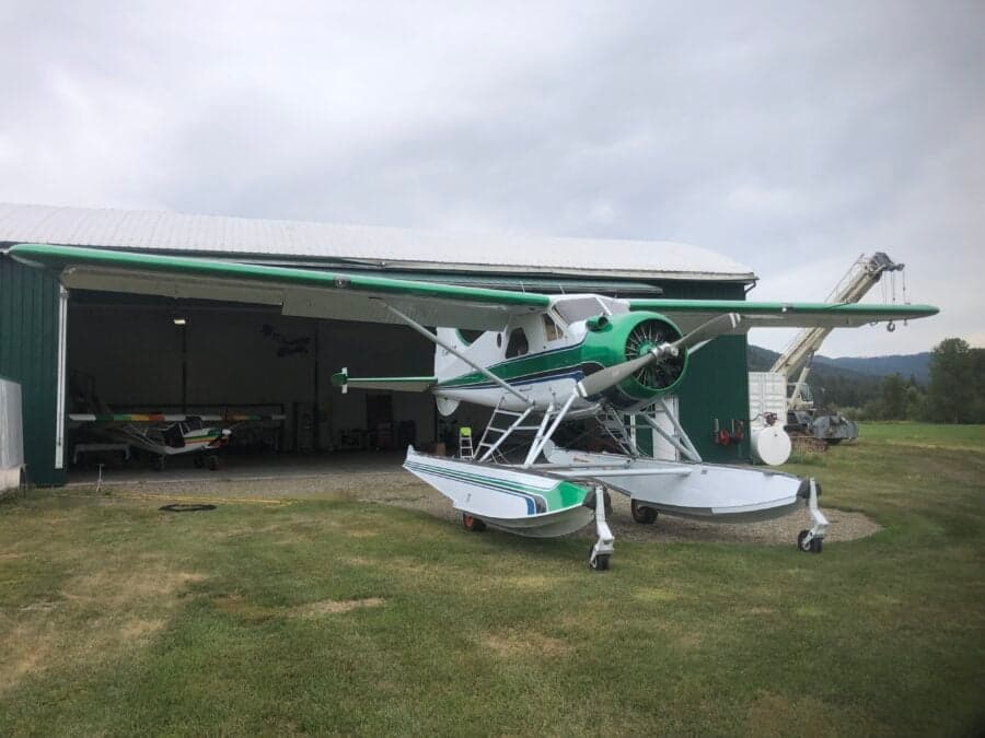 Side view of a green and white float plane parked in front of a hangar.