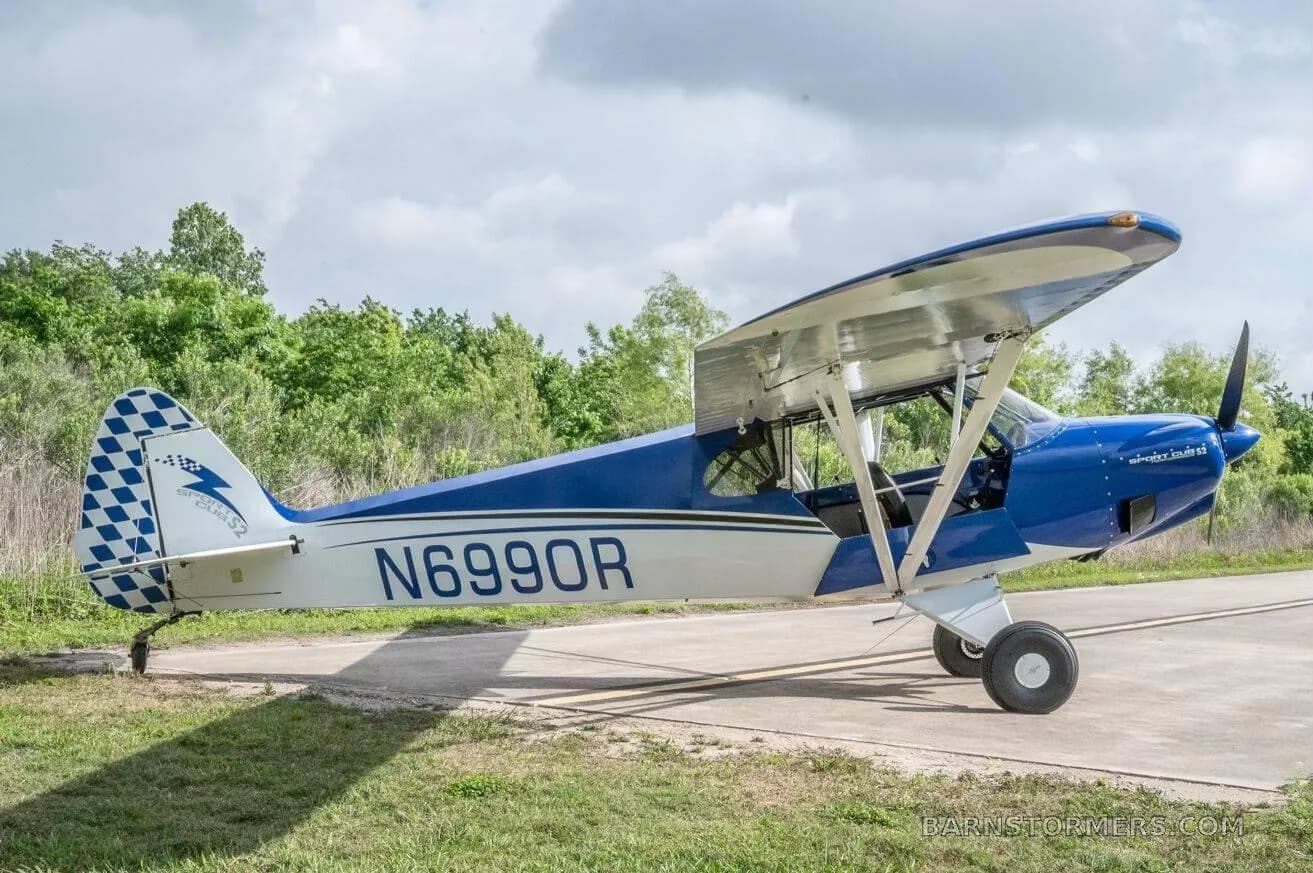 A blue and white single-engine taildragger aircraft (N6990R) with a checkered tail is parked on a concrete pad.