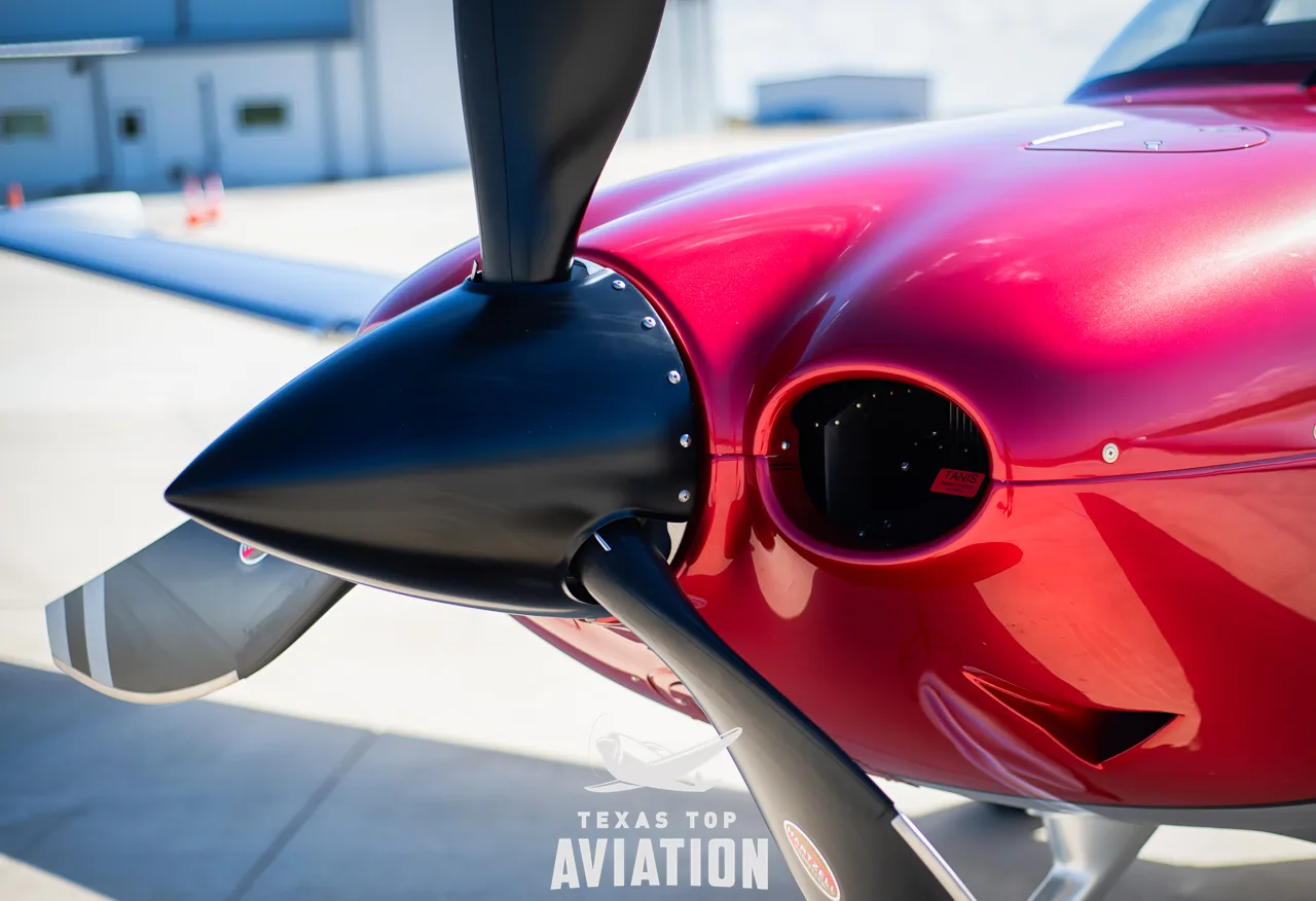 A close-up view of the red cowling and black propeller of a Cirrus SR22T GTS aircraft from the side.