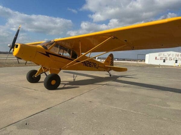Side view of a yellow Legend Cub aircraft with registration N267RJ on the fuselage, parked on an airfield.