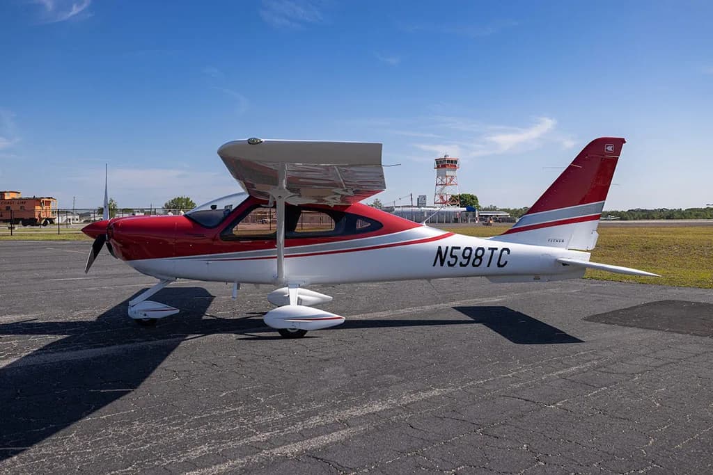 A side view of a red and white Tecnam P2010 aircraft with registration N598TC parked on an airfield.