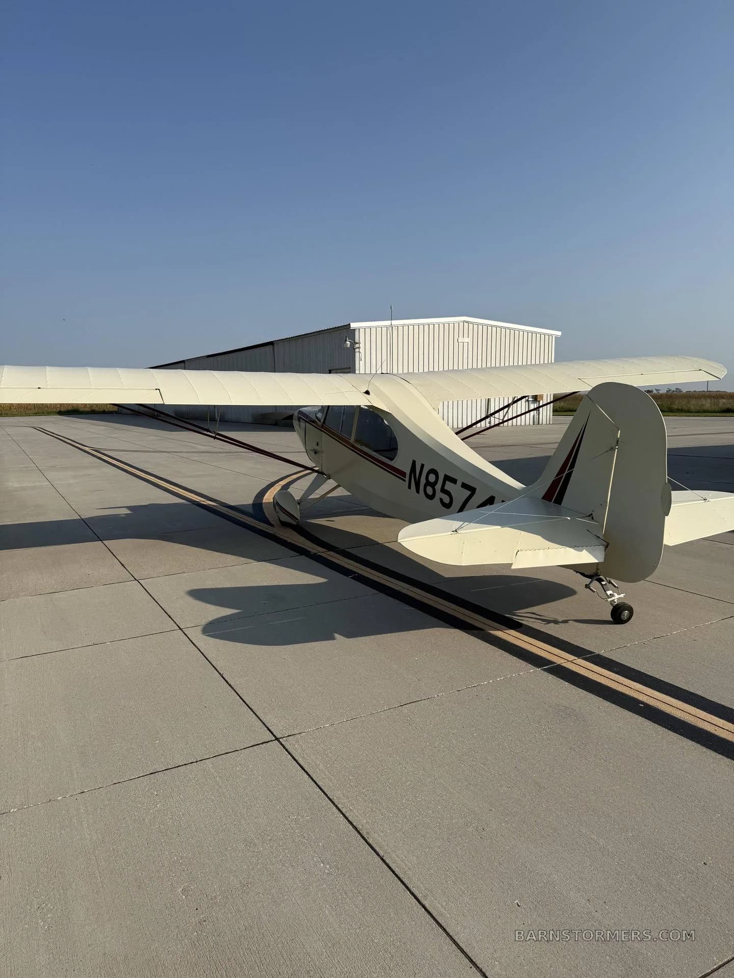 A cream-colored, high-wing taildragger aircraft, registration N85745, parked on a tarmac with a white hangar in the background.
