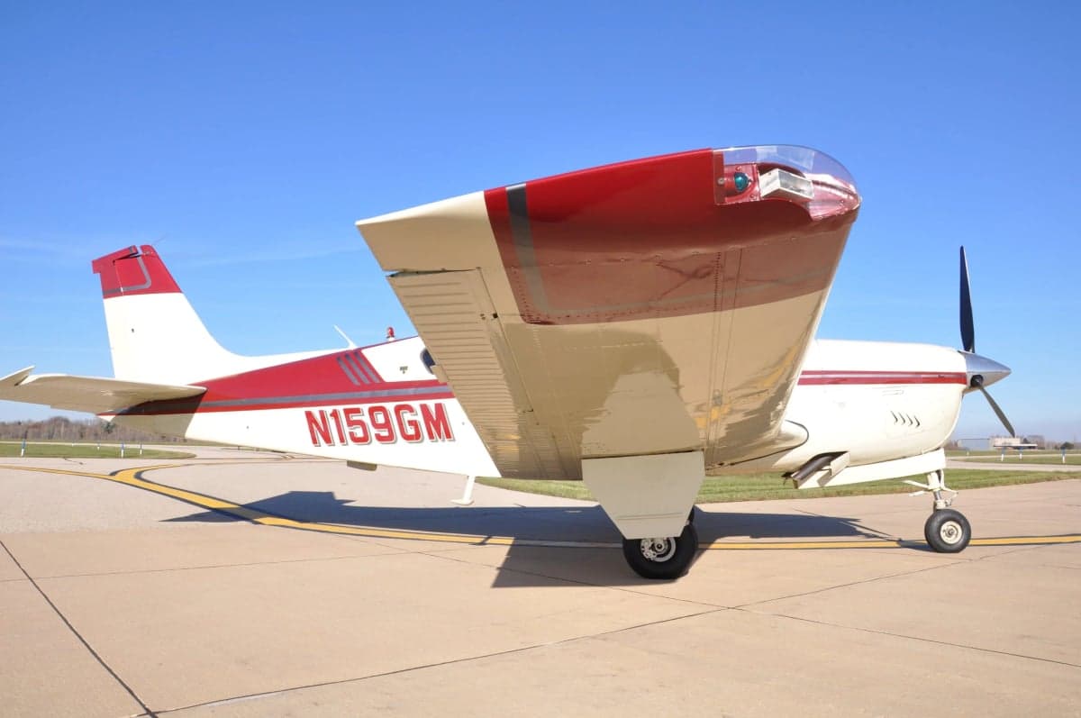 Side view of a Beechcraft Bonanza with a red and white paint scheme on the tarmac.