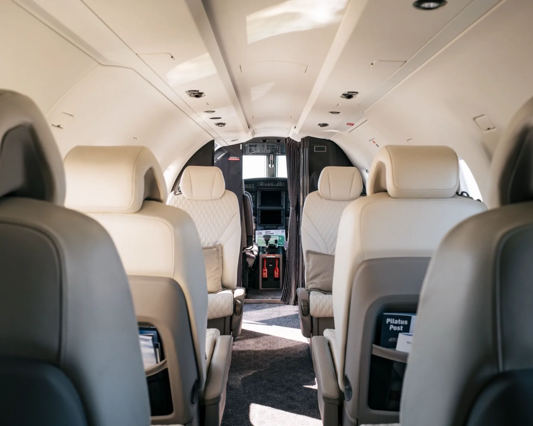 The aircraft cabin interior with light-colored seats, looking forward towards the cockpit area.