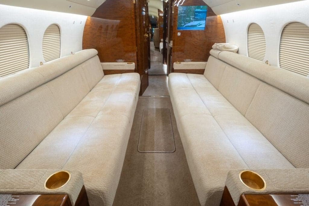 The aircraft's interior features tan leather seats, a wood table with a wine bottle, and a flower arrangement.