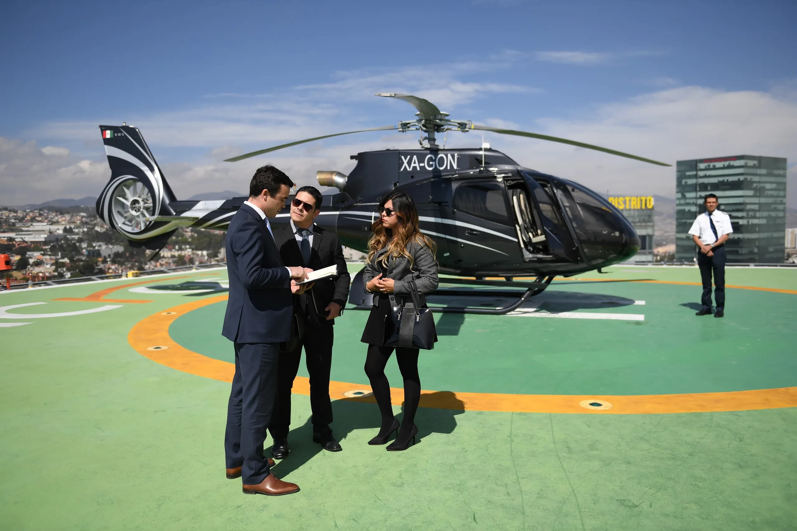 Black helicopter on a helipad with people standing nearby.