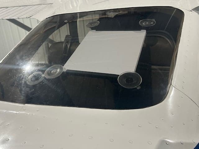 A close-up view of the rear window of a white aircraft, showing a white panel held by suction cups.