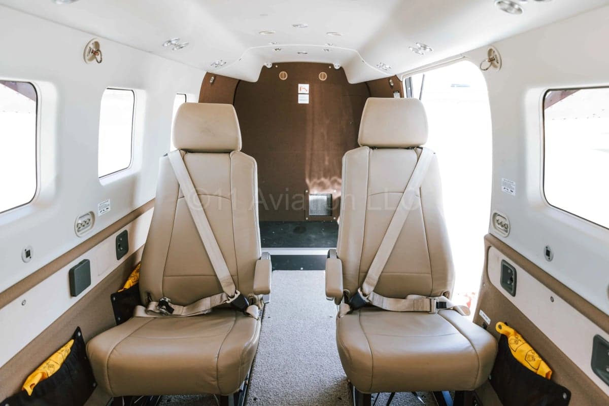 The interior cabin of the aircraft, showing two rows of beige leather seats with seatbelts.