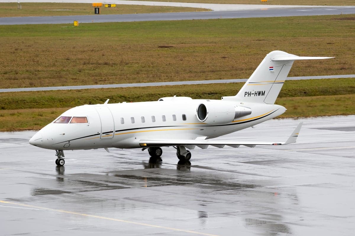 A white private jet with Dutch registration PH-HWM parked on a wet tarmac.