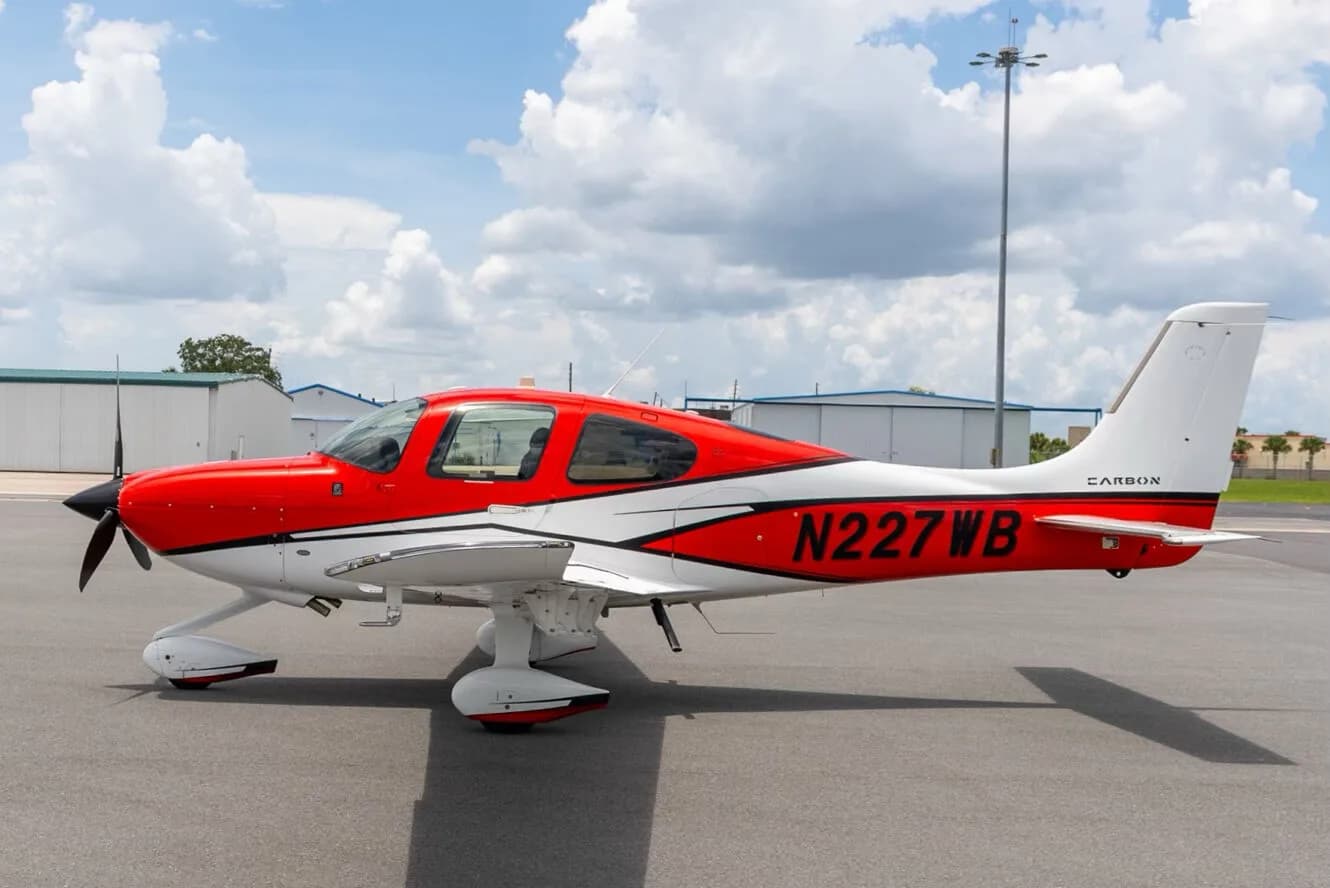A red and white Cirrus SR22 aircraft with registration N227WB parked on an airfield, viewed from the side.